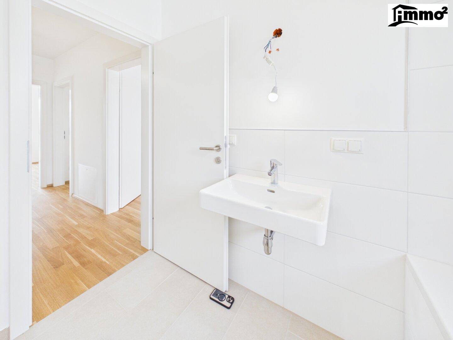 Modernes Badezimmer mit Waschbecken und weiß gefliesten Wänden, mit Blick in den angrenzenden Flur.
