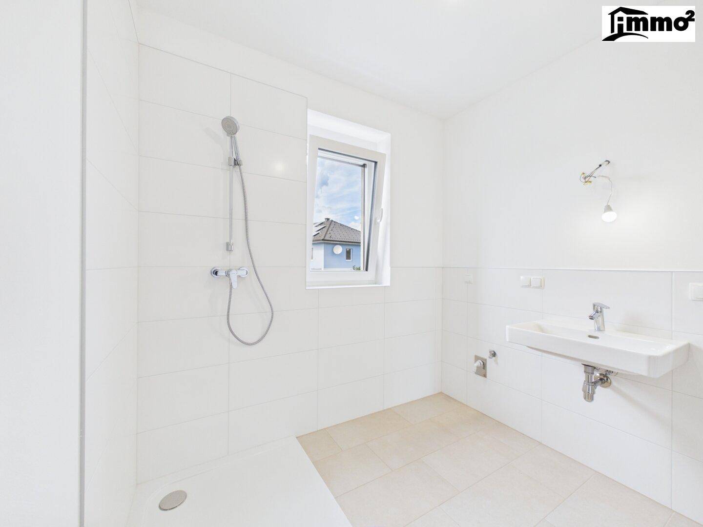 Helles Badezimmer mit Duschbereich, Waschbecken und Fenster, komplett in Weiß gefliest.