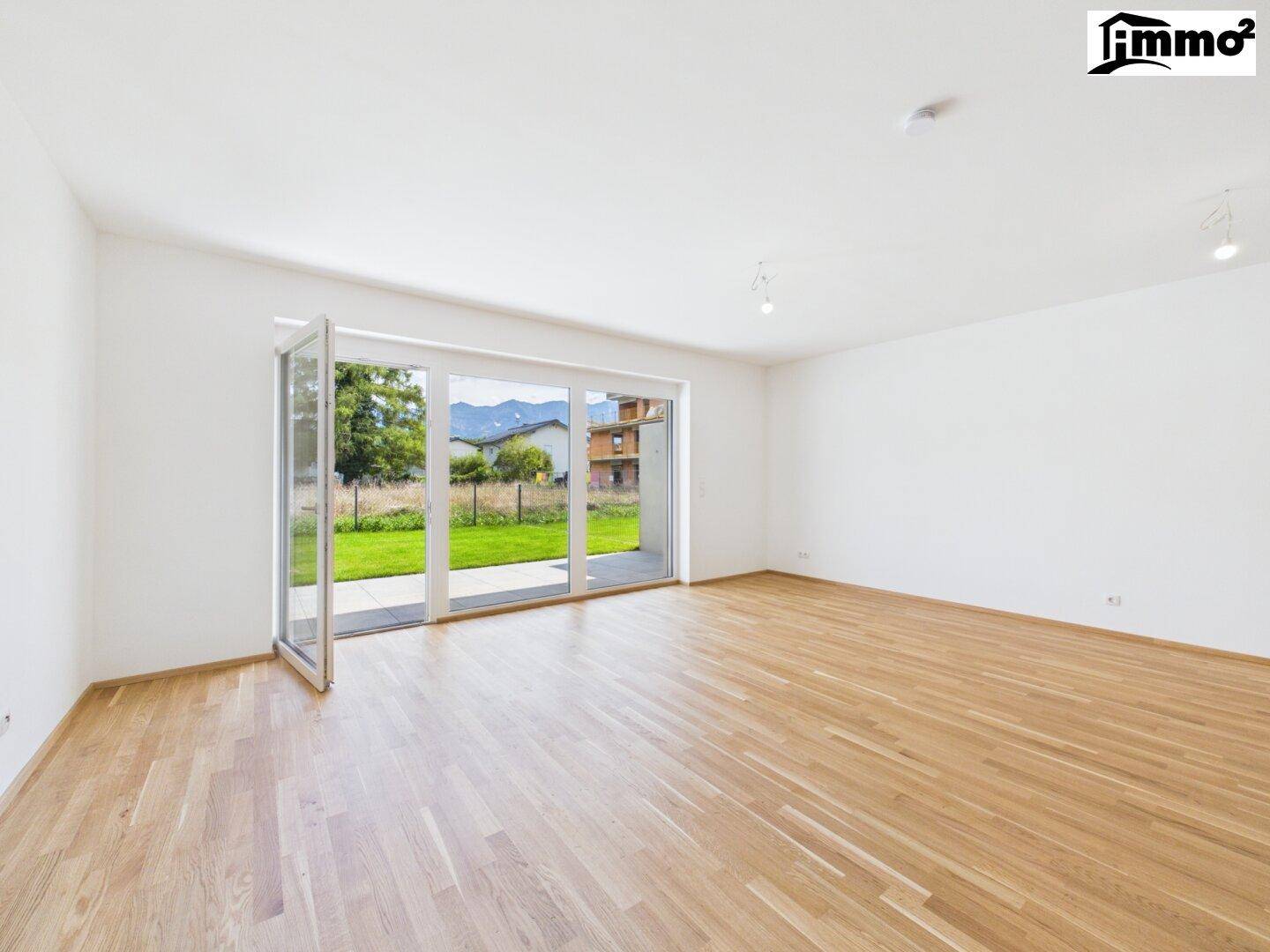 Helles Wohnzimmer mit Holzboden und großen Fenstern, die einen weiten Blick in den Garten ermöglichen.