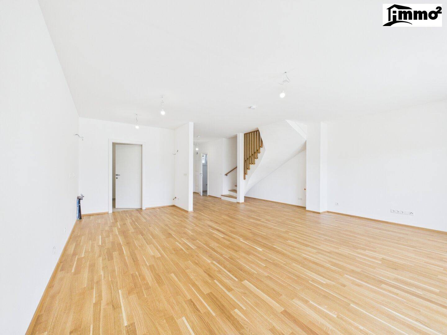 Geräumiger offener Wohnbereich mit Holzboden und einer eleganten Holztreppe, die in die obere Etage führt.