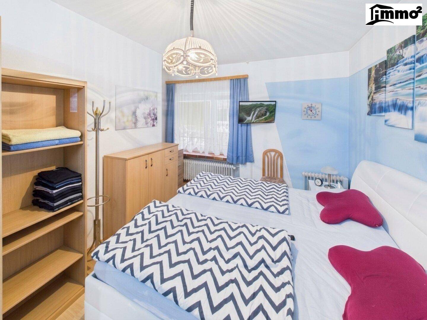 Helles Schlafzimmer mit zwei Einzelbetten, blauer Wandgestaltung und Blick ins Grüne.