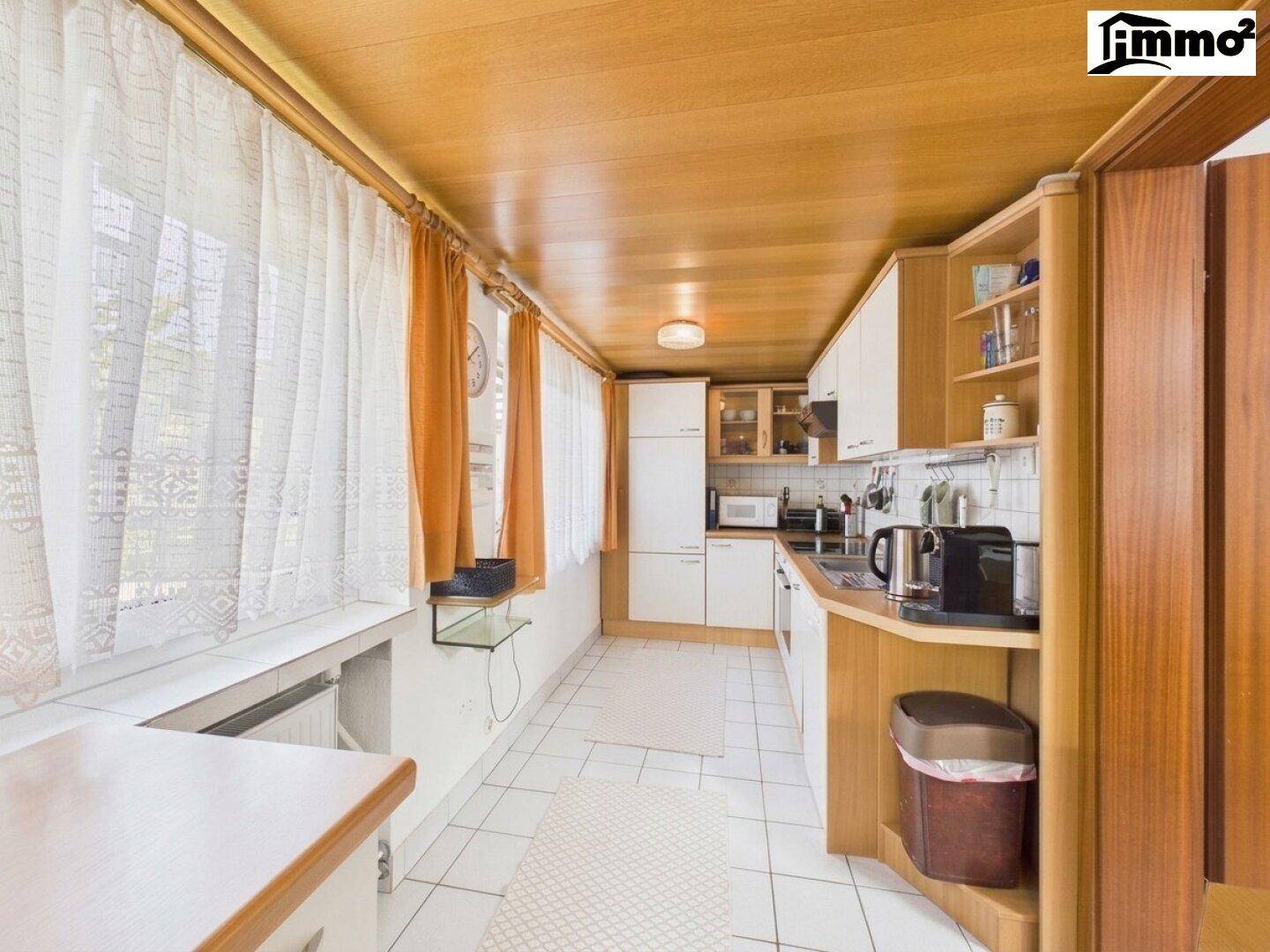 Schmale Küche mit Holzdecke, weißen Einbauschränken und einem Fenster für Tageslicht.