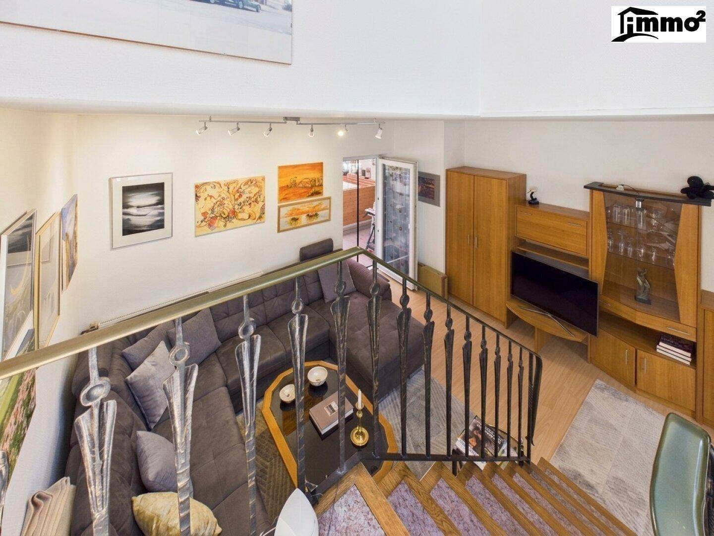 Blick von der Wendeltreppe in das Wohnzimmer mit großer Couch und Zugang zum Balkon.