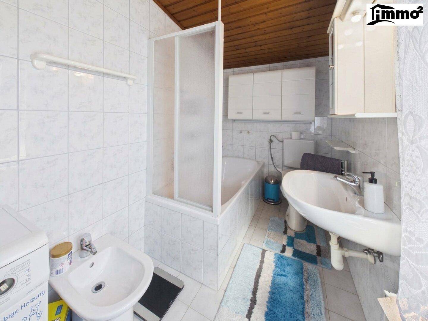 Gefliestes Badezimmer mit Badewanne, Duschabtrennung, Waschbecken, Bidet und Waschmaschine.
