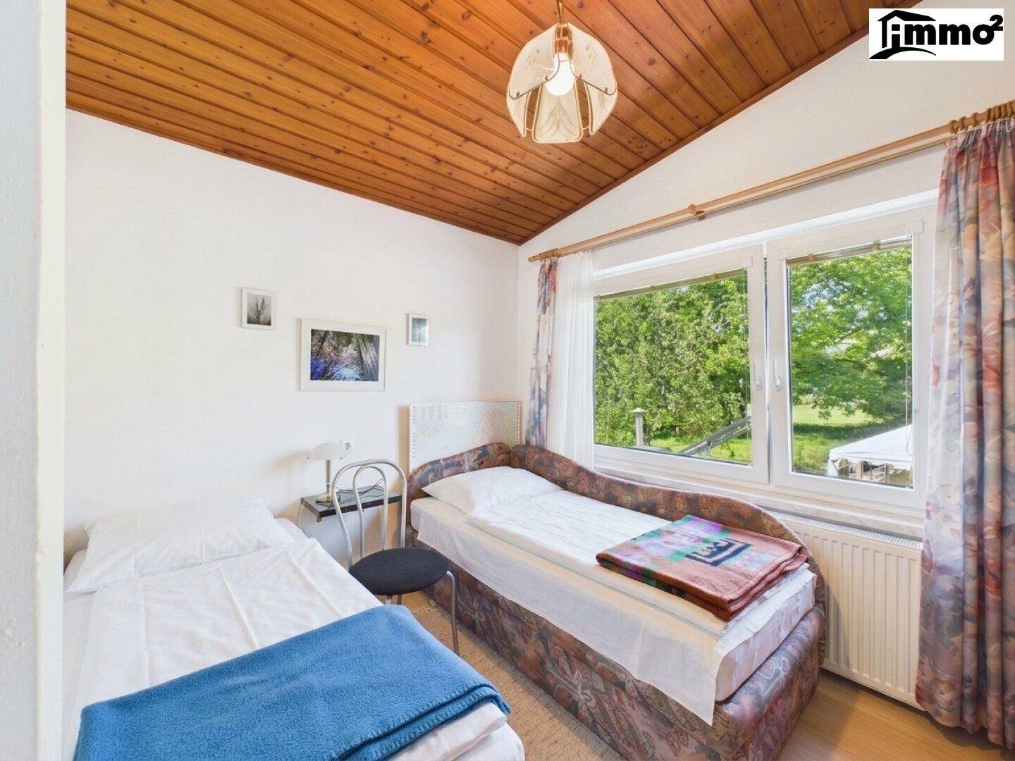 Helles Schlafzimmer mit zwei Einzelbetten, Holzdecke und einem Fenster mit Blick ins Grüne.