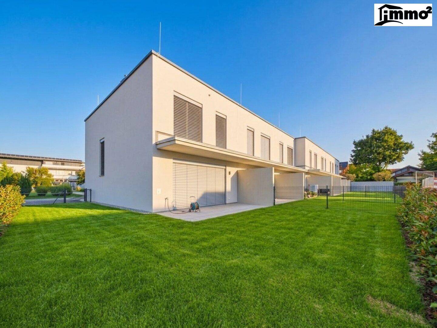 Hinteransicht moderner Reihenhäuser mit gepflegtem Rasen und klarem Himmel.