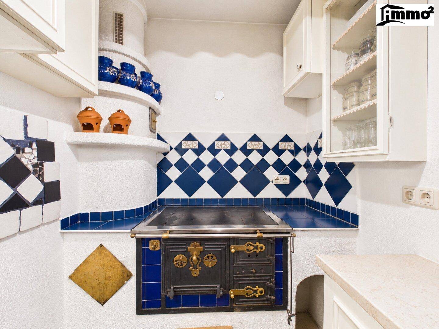 Traditionelle Küche mit Kachelofen, blauen Fliesen und weißen Schränken im Landhausstil.