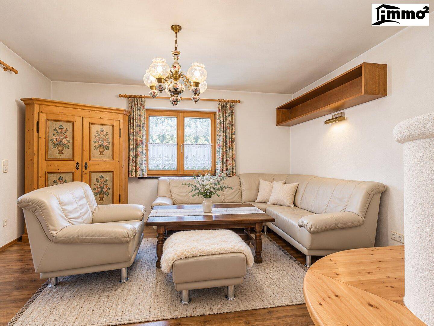 Gemütliches Wohnzimmer mit beiger Ledercouch, Holztisch und traditionellem Kachelofen.