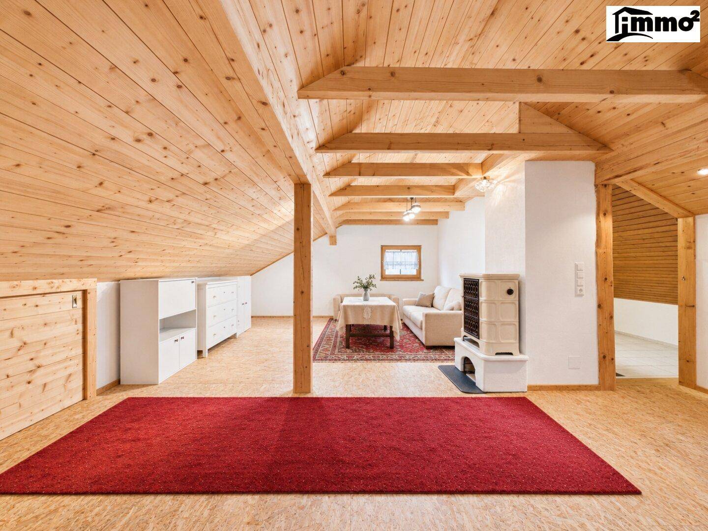 Offener Wohnbereich im Dachgeschoss mit Holzbalken, Holzboden und Kachelofen.