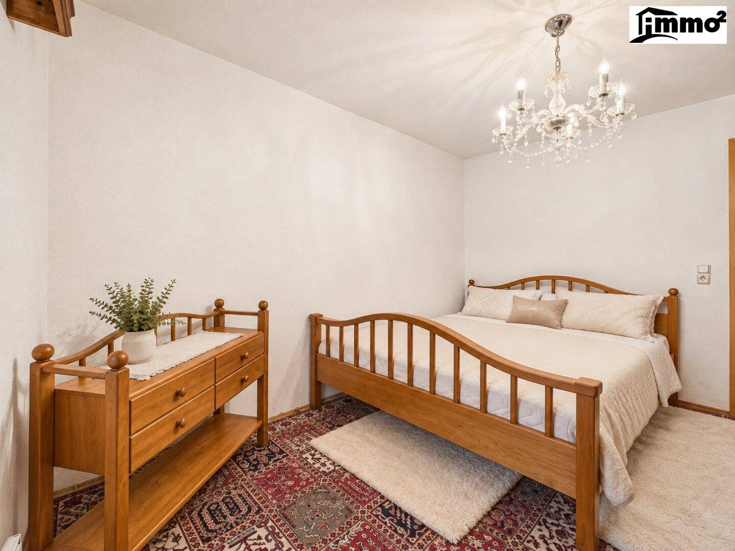 Schlafzimmer mit Holzbett, Kronleuchter und traditionellem Teppichboden.