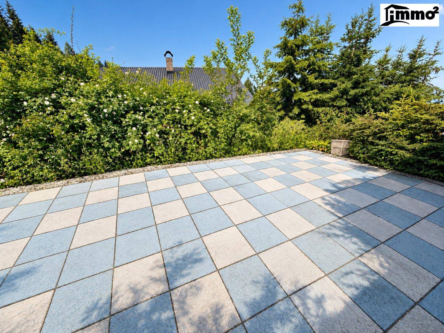 Große gepflasterte Terrasse mit blau-weißen Fliesen und umgebender Hecke.