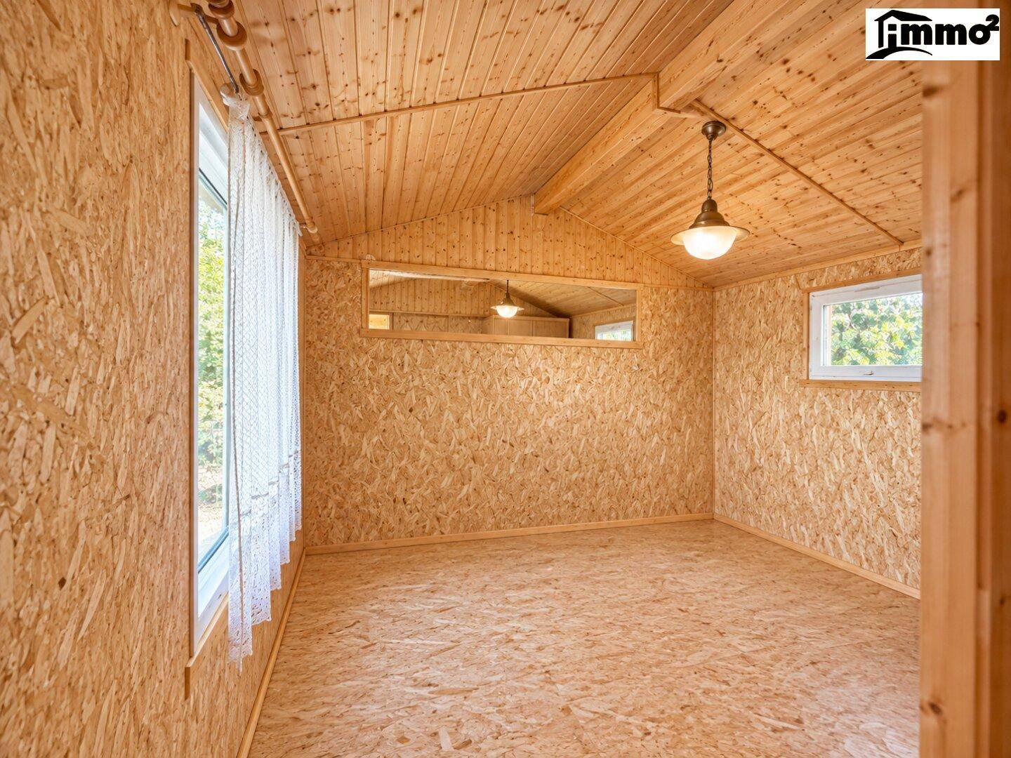 Kleiner Raum mit Holzwänden und -decke, großen Fenstern und Holzboden.