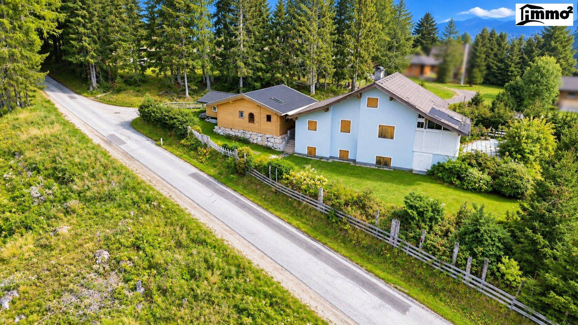 Luftaufnahme eines Hauses mit Holzanbau und umgebender Natur in den Bergen.