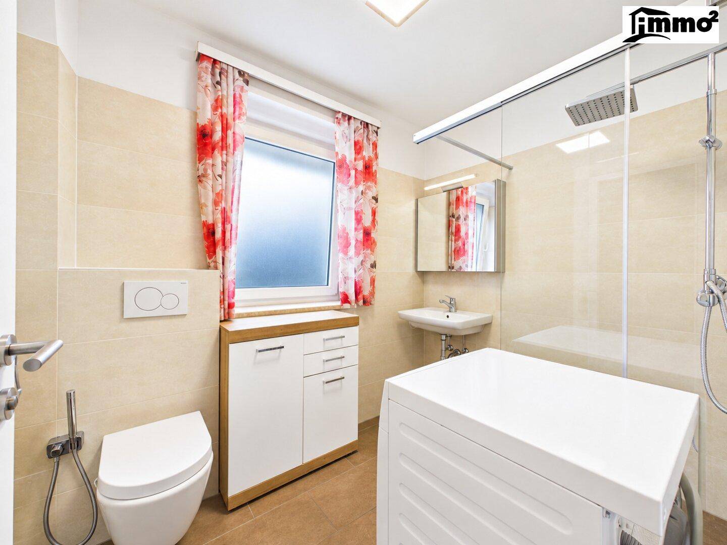 Helles Badezimmer mit Dusche, WC, Waschmaschine und Fenster.