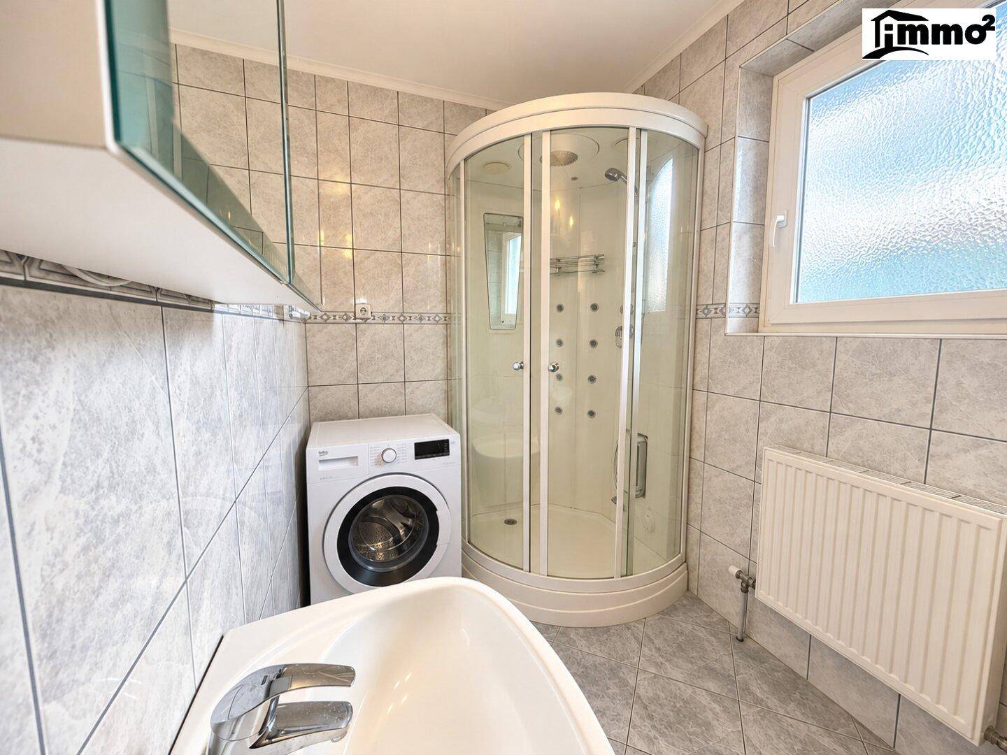 Badezimmer mit Duschkabine, Waschmaschine und hellen Fliesen.
