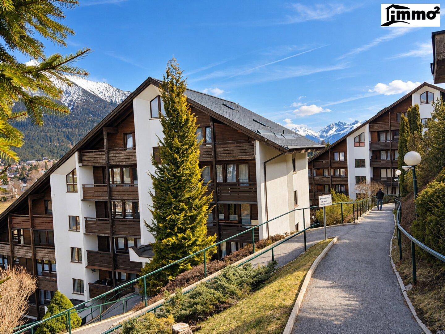 Mehrere Gebäude im alpinen Stil mit Holzbalkonen und schneebedeckten Bergen im Hintergrund.