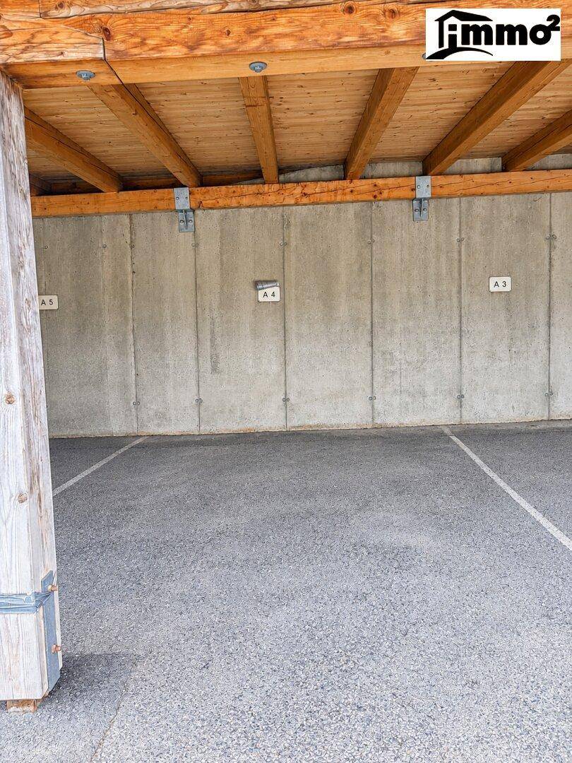 Überdachter Parkplatz mit Holzbalkendecke und Betonwänden, nummerierte Stellplätze.