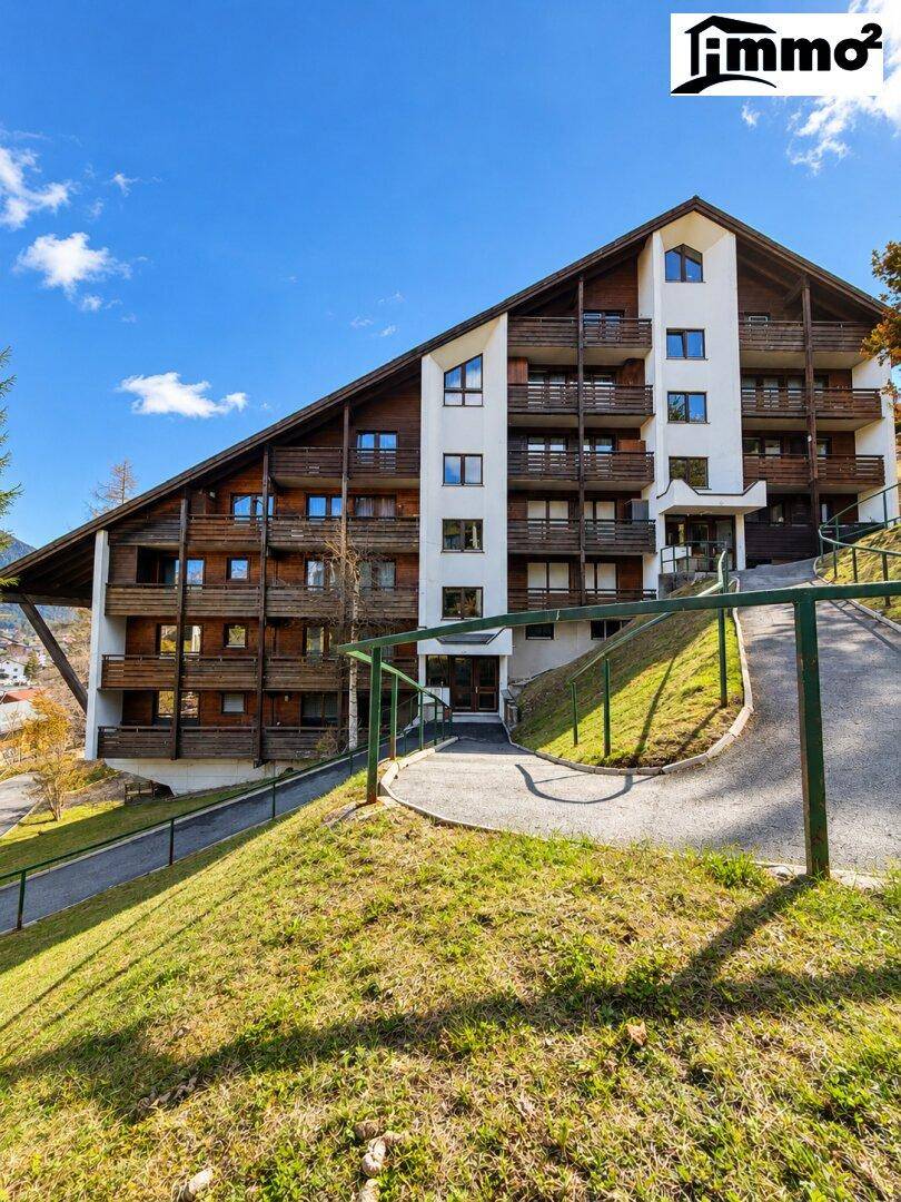 Frontansicht eines Gebäudes im alpinen Stil mit Holzbalkonen und einem grünen Hang im Vordergrund.