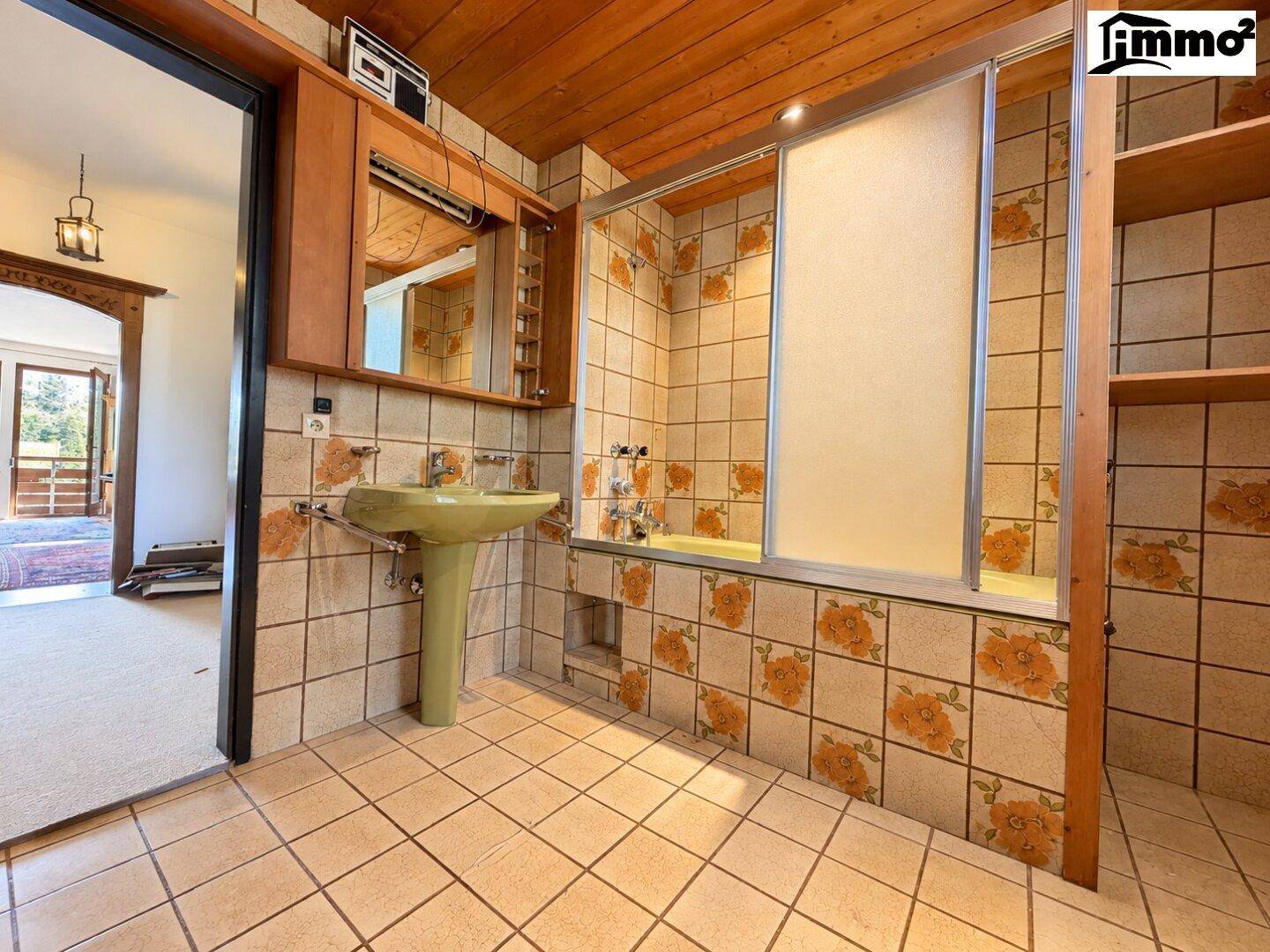 Badezimmer mit floralen Fliesen, grünem Waschbecken und Badewanne mit Duschabtrennung.