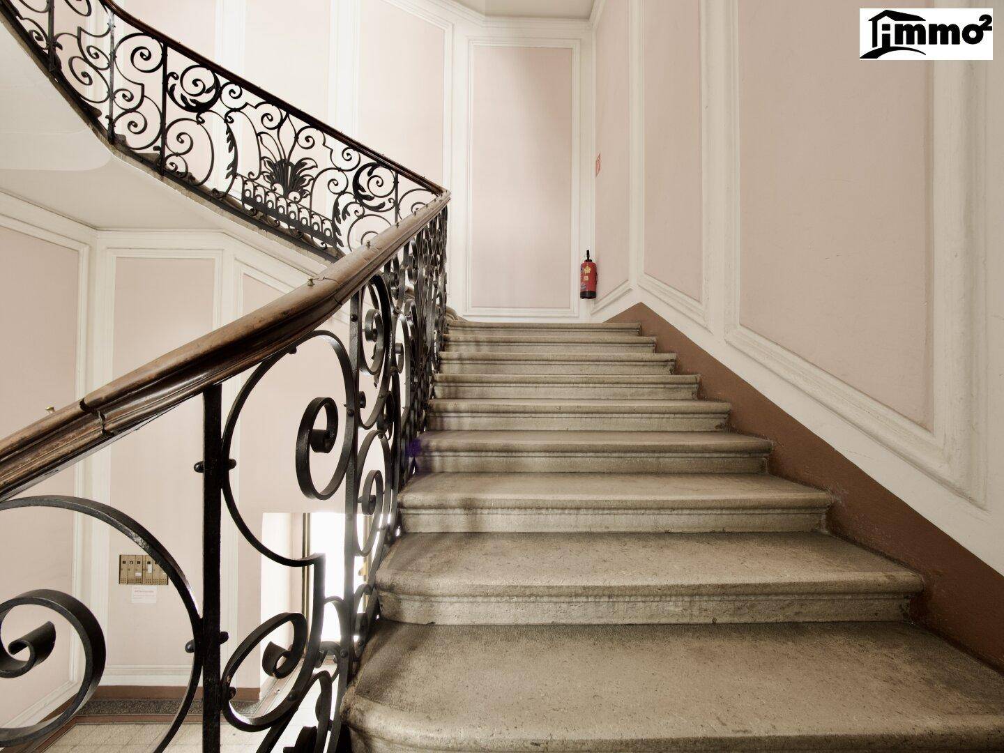 Elegantes Treppenhaus mit geschwungenem schmiedeeisernem Geländer und Steinstufen in einem Altbau.