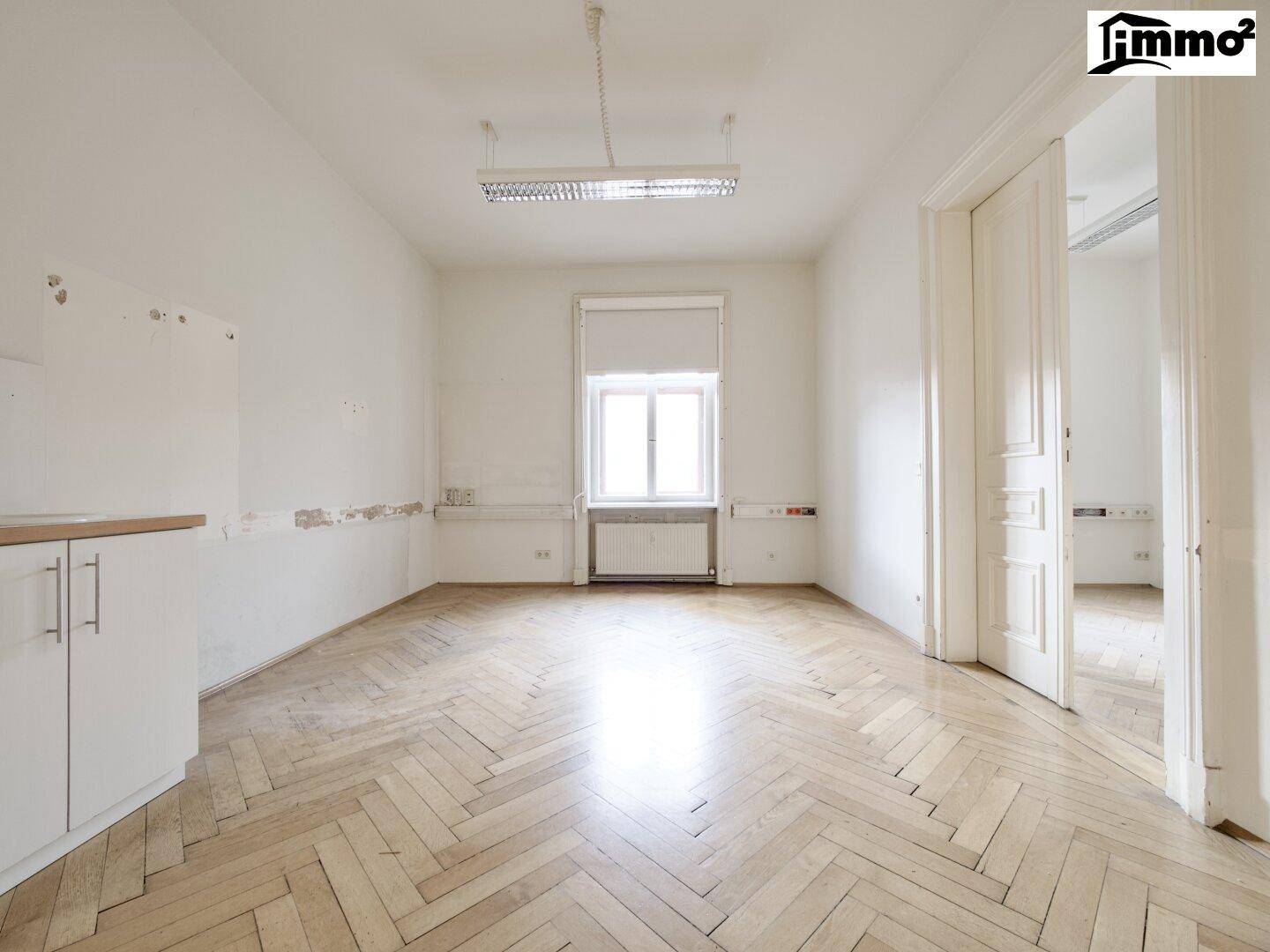 Heller Raum mit Fischgrätparkett, einem Fenster und einer kleinen Arbeitsfläche, möglicherweise für eine Teeküche.