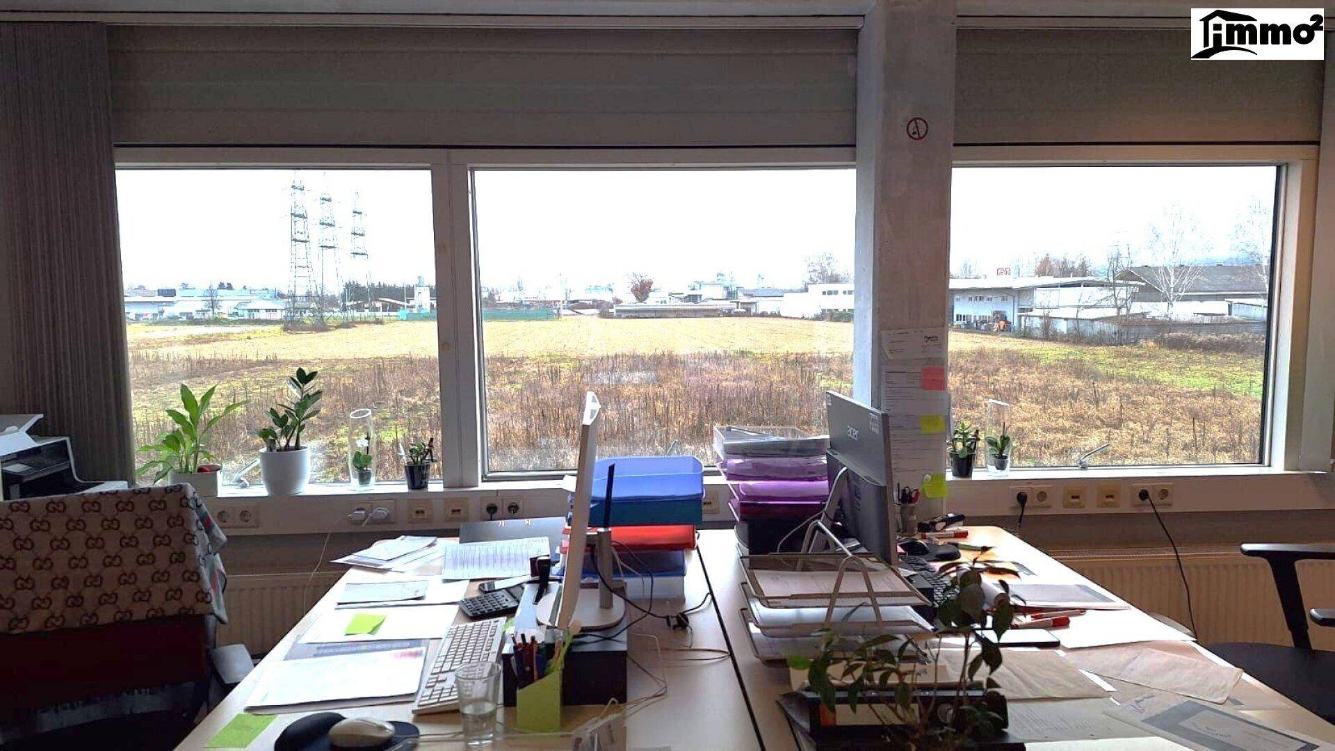 Büroarbeitsplatz mit Blick auf eine weite, offene Fläche und Industriegebäude in der Ferne.