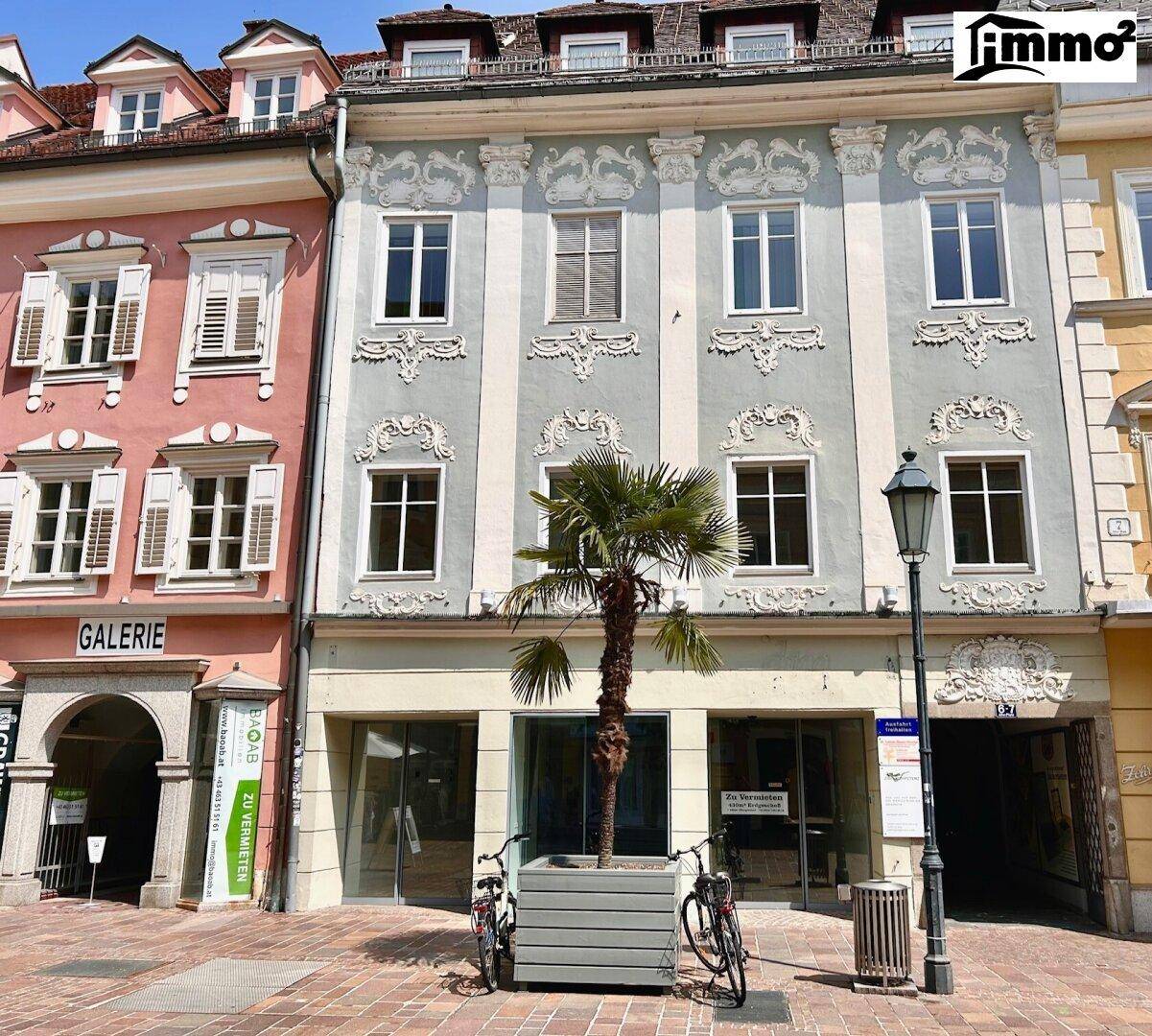Detailansicht einer historischen Fassade mit Stuckverzierungen, großen Fenstern und einem Geschäft im Erdgeschoss.