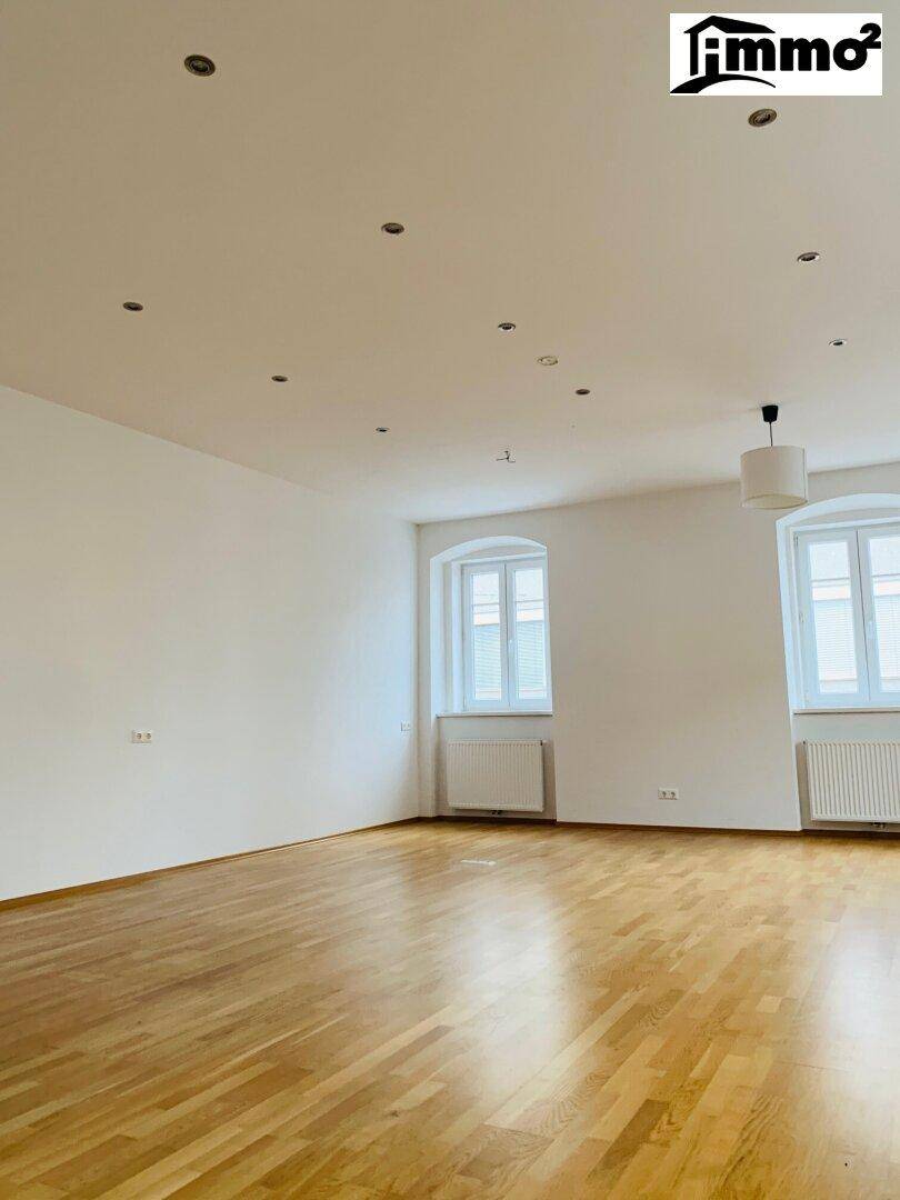 Geräumiger, heller Wohnraum mit Parkettboden, zwei Fenstern und integrierter Deckenbeleuchtung.
