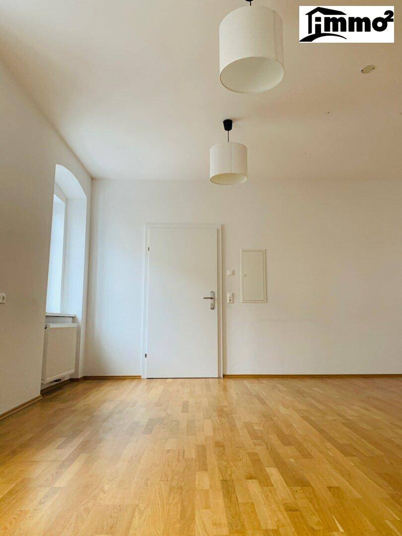 Heller Raum mit Parkettboden, einer weißen Tür und einem Fenster, das viel Tageslicht hereinlässt.
