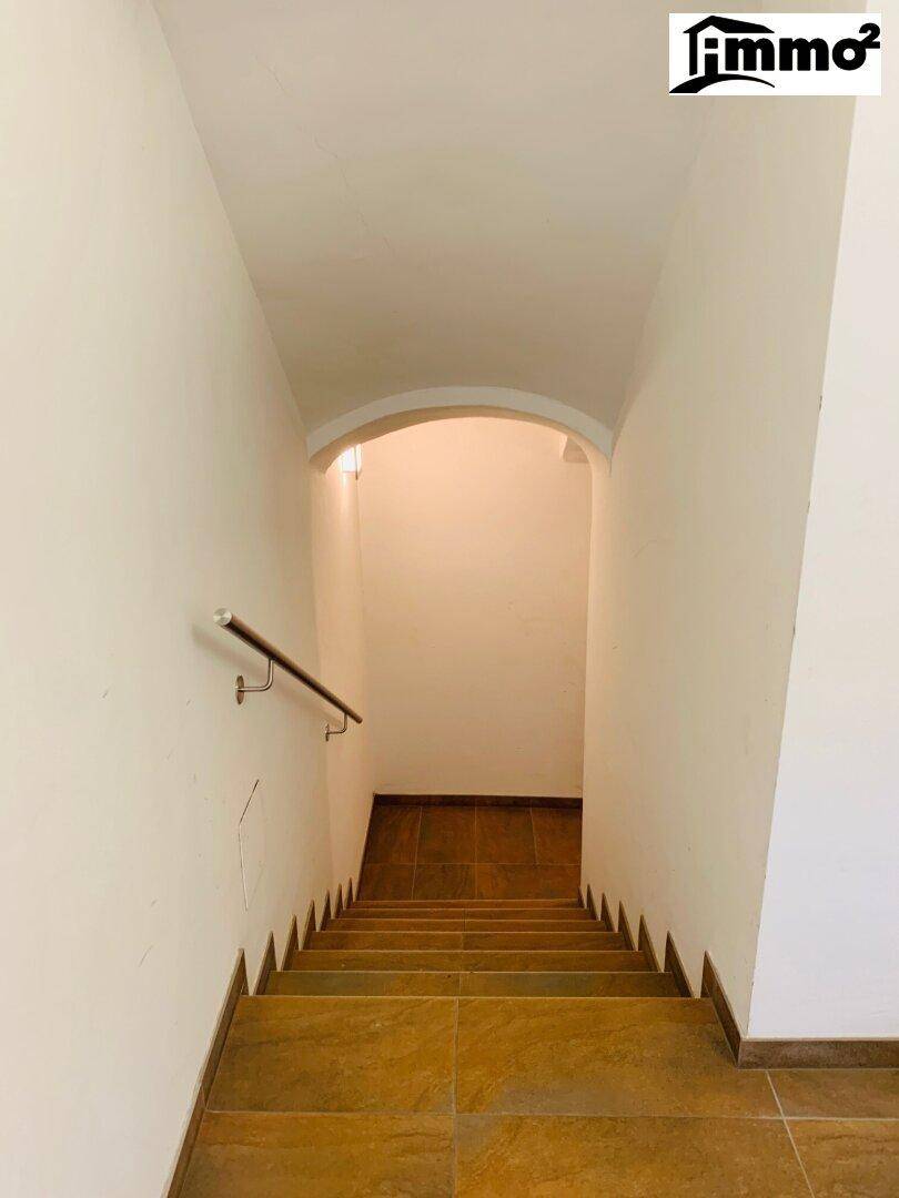 Treppenhaus mit gefliesten Stufen und einem schlichten Metallgeländer, das in einen gewölbten Bereich führt.