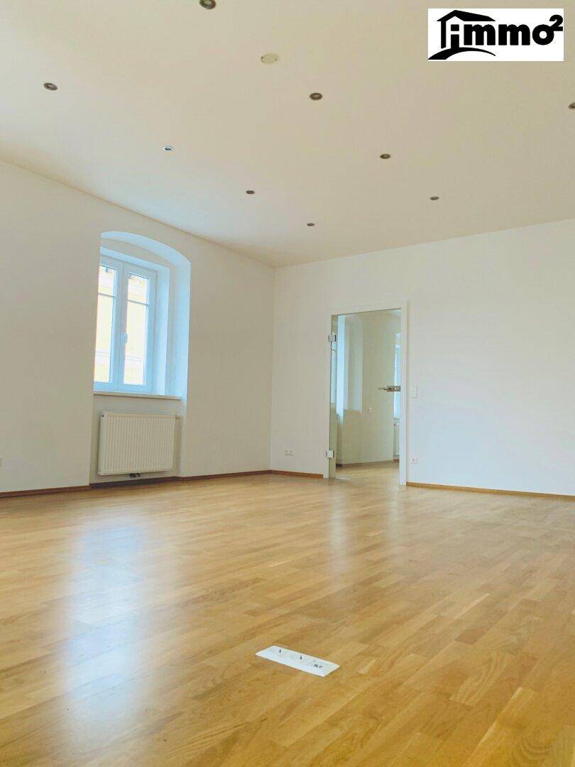 Freundlicher Raum mit Holzparkett, einem großen Fenster und einer modernen Glastür zu einem Nebenraum.