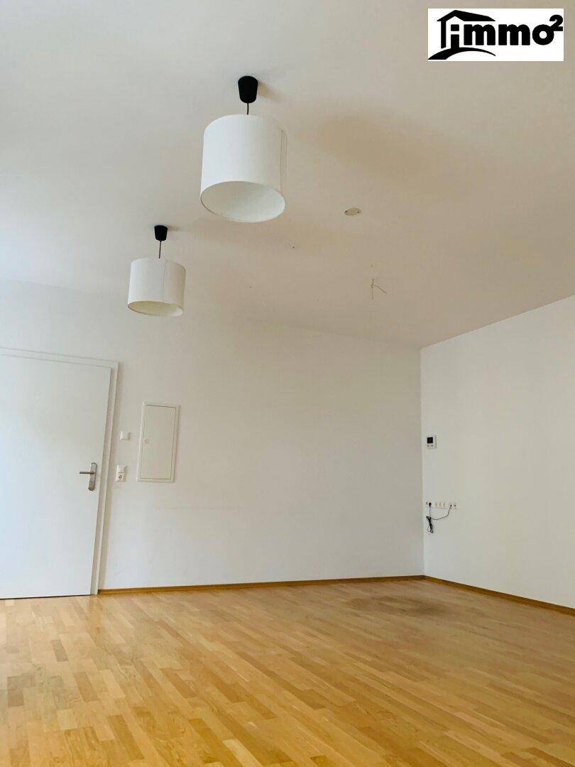 Leerer Raum mit hellem Holzfußboden und weißen Wänden, ausgestattet mit zwei Deckenleuchten.