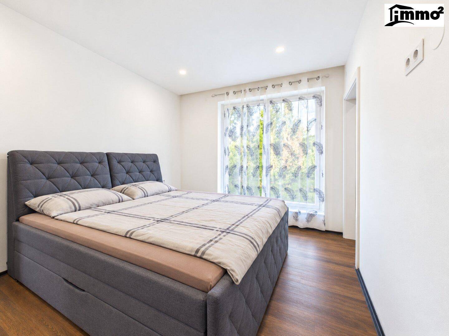 Helles Schlafzimmer mit großem Doppelbett, Holzboden und Fenster mit Vorhängen.