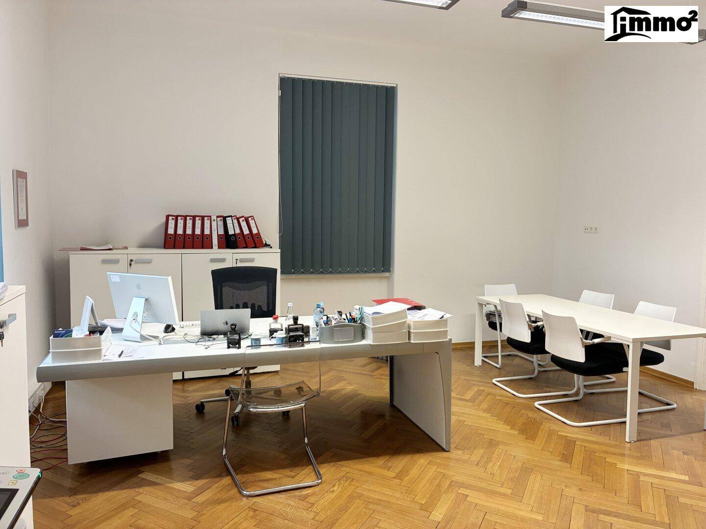 Geräumiges Büro mit großem Schreibtisch, Konferenztisch und Fenster mit Jalousien.