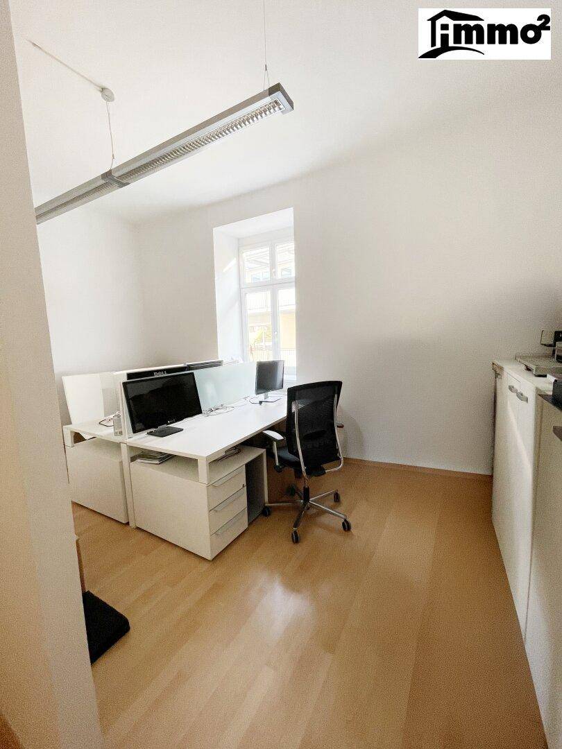 Helles Büro mit mehreren Arbeitsplätzen, einem Fenster und funktionaler Einrichtung.