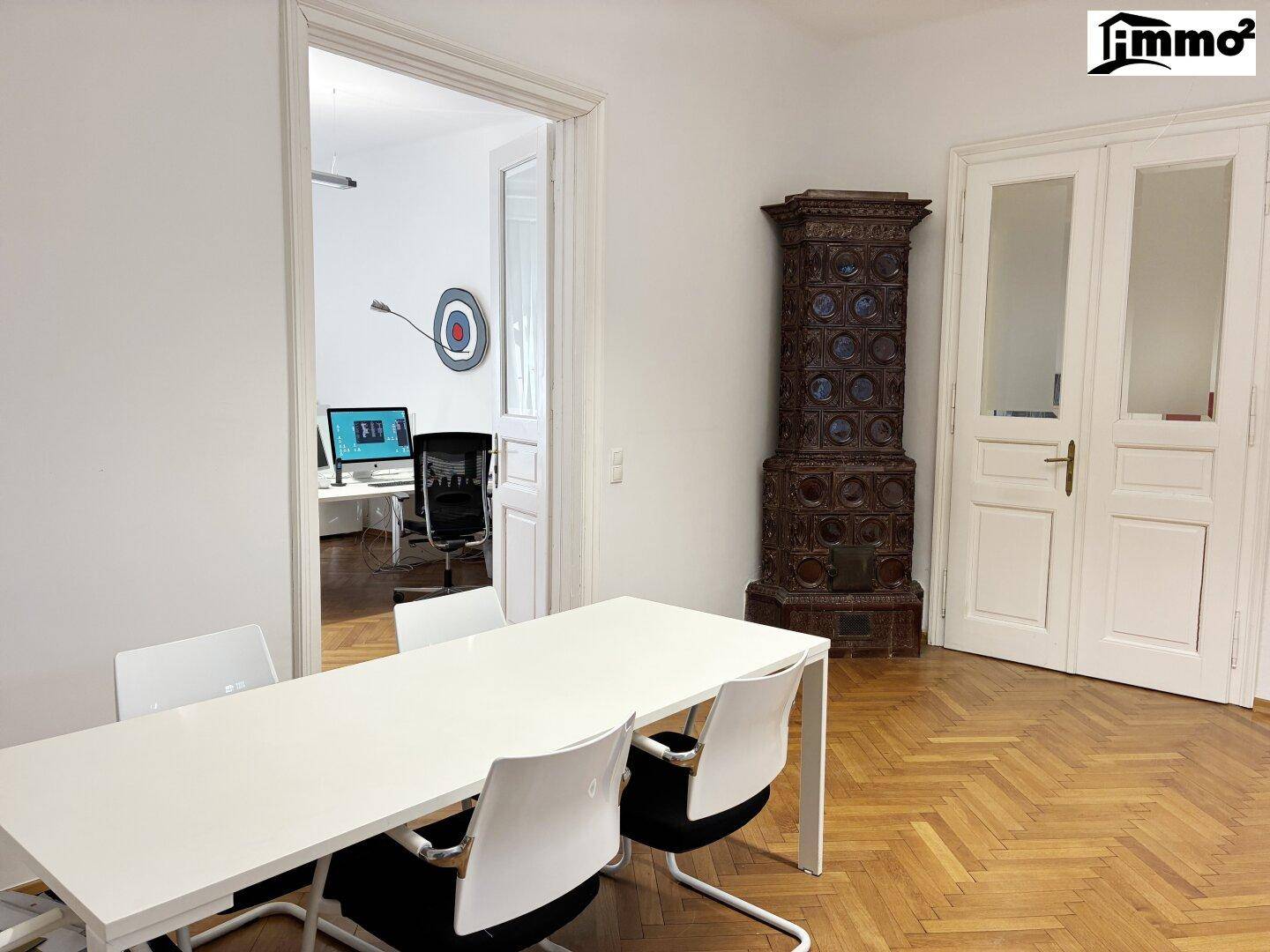 Konferenzraum mit großem Tisch, historischem Kachelofen und Zugang zu einem weiteren Büro.