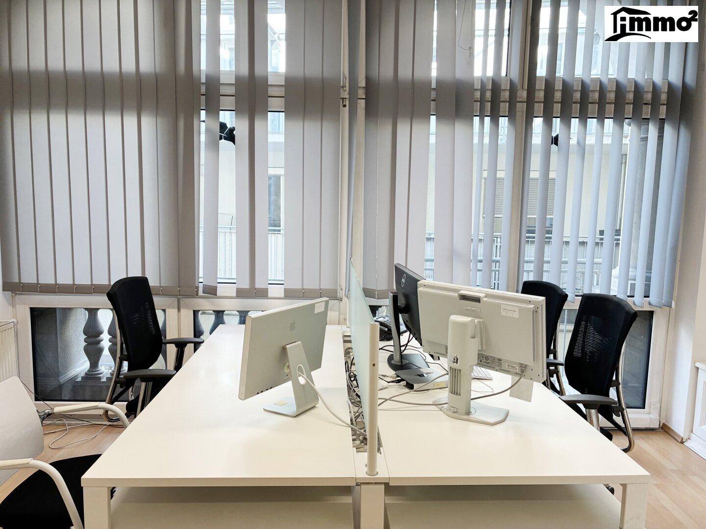 Arbeitsplätze in einem Büro mit großen Fenstern und vertikalen Jalousien für Privatsphäre.