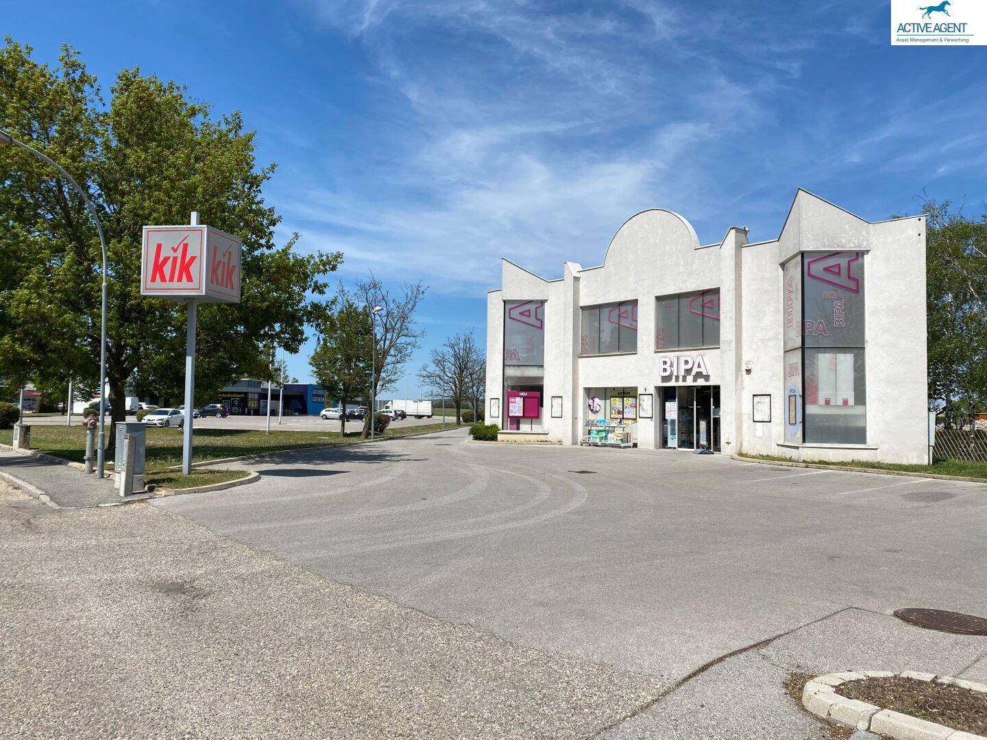 Geschäftsgebäude mit Parkplatz und einem KiK-Schild, umgeben von Bäumen.