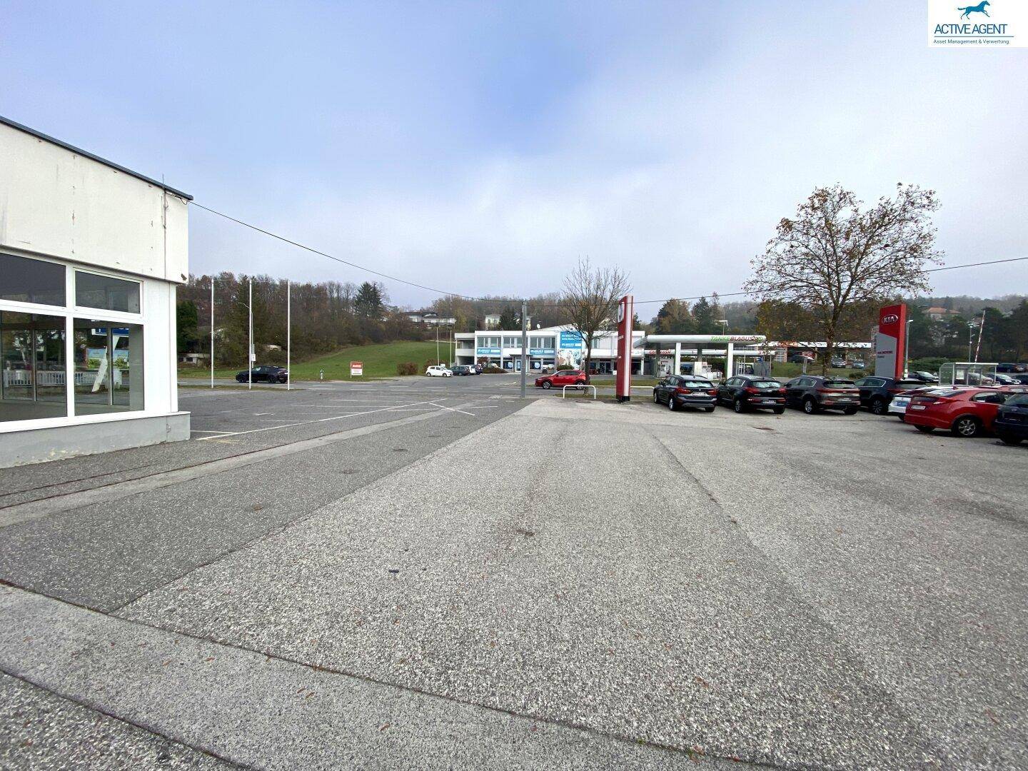 Großer Parkplatz vor dem Geschäftsgebäude mit Blick auf die umliegenden Gewerbeflächen und die Straße.