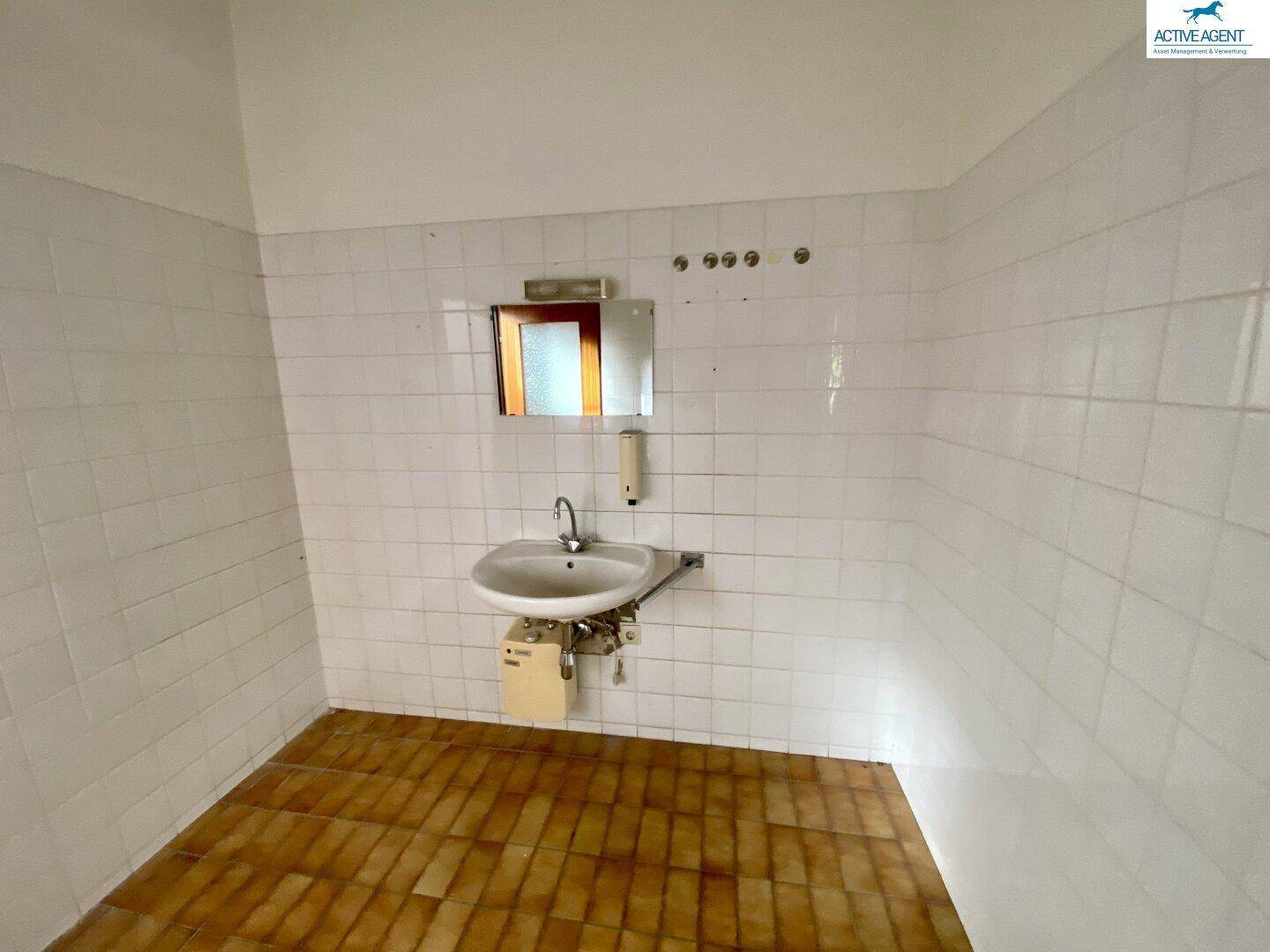 Einfacher Waschraum mit Fliesen an den Wänden und einem Waschbecken, funktional und sauber.