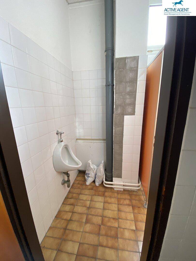 Herren-WC mit Urinal und gefliestem Boden, in einem funktionalen und sauberen Zustand.