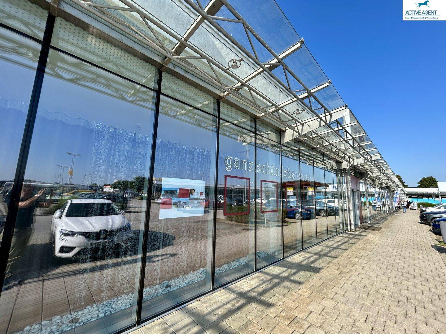 Moderne Glasfassade eines Gewerbegebäudes mit weitreichenden Reflexionen und einem transparenten Vordach.