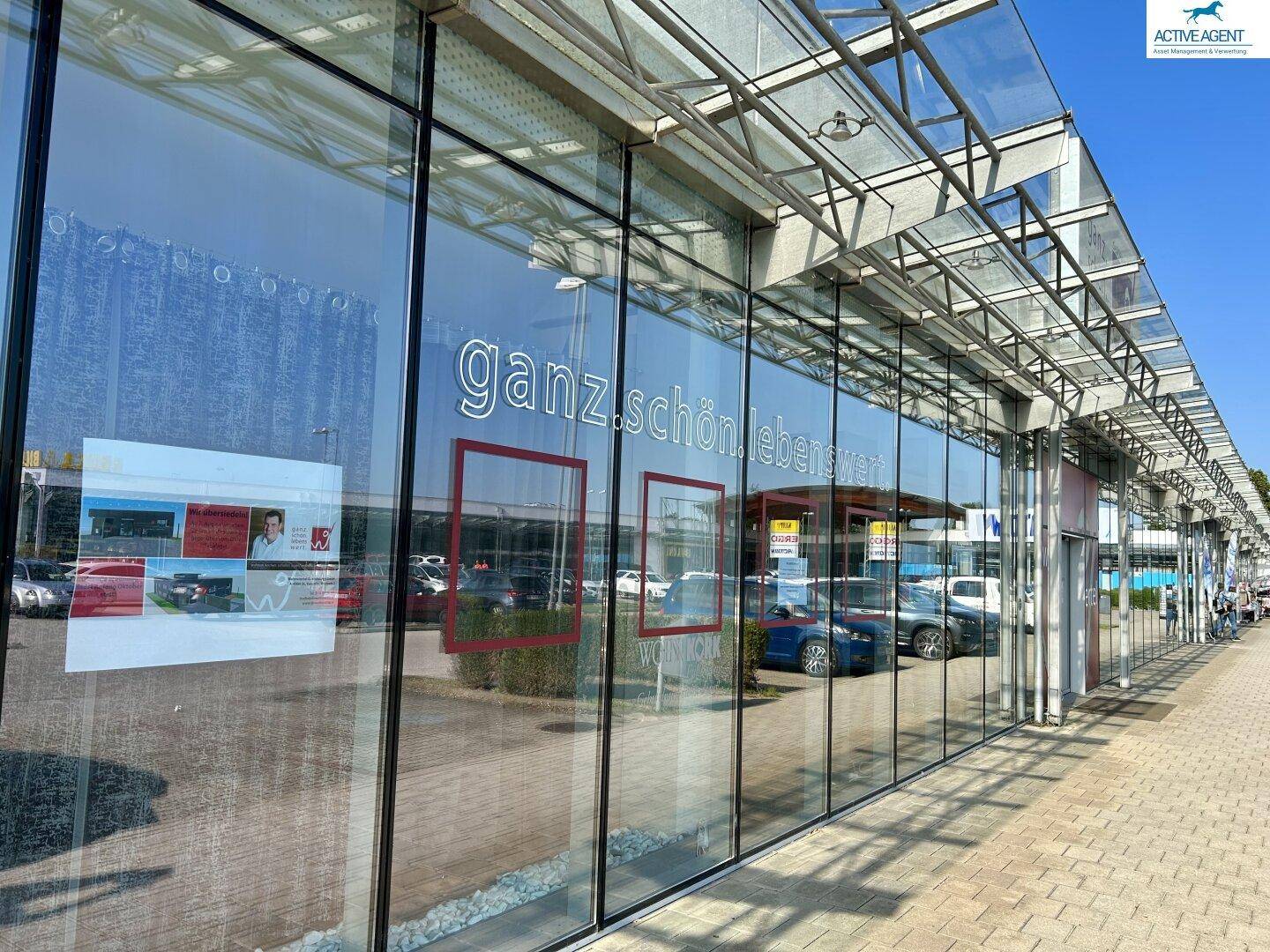 Lange Glasfassade eines modernen Geschäftsgebäudes mit reflektierenden Fenstern und einem schützenden Vordach.