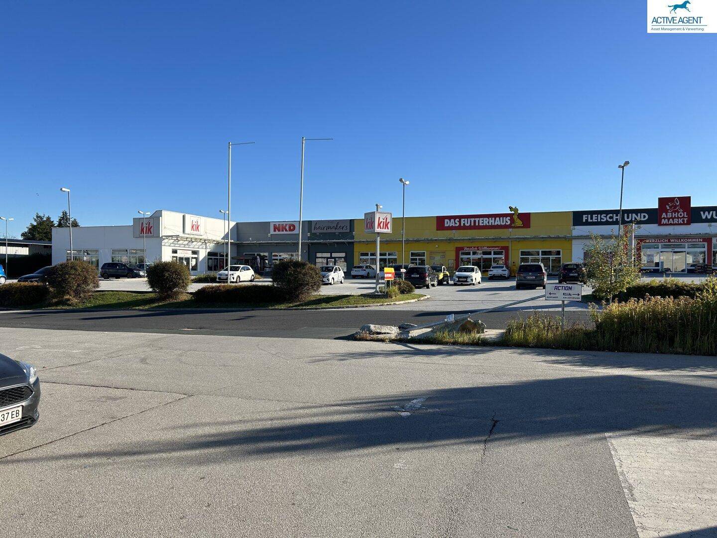Weitläufige Außenansicht des gesamten Fachmarktzentrums mit verschiedenen Geschäften und einem großen Parkplatz.
