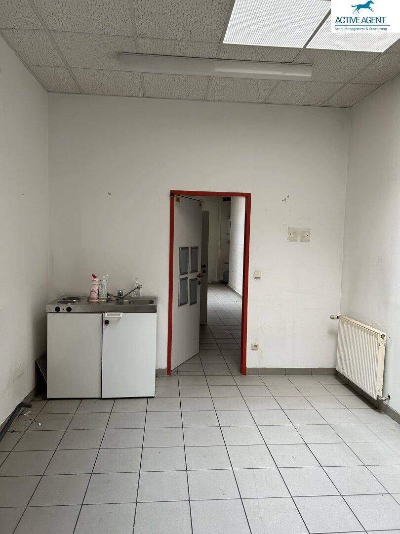 Kleiner, gefliester Raum mit einer Küchenzeile, Heizkörper und einer Tür, die zu einem weiteren Bereich führt.
