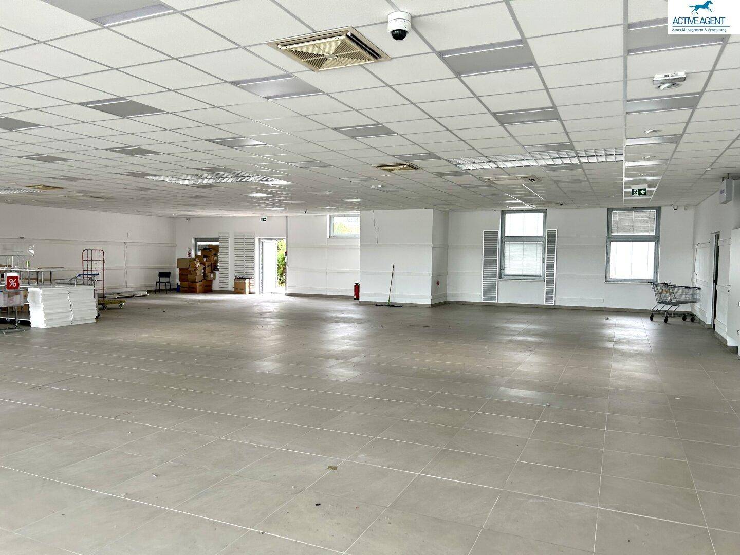 Großer, leerer Verkaufsraum mit Fliesenboden, abgehängter Decke und natürlichem Lichteinfall durch die Fenster.