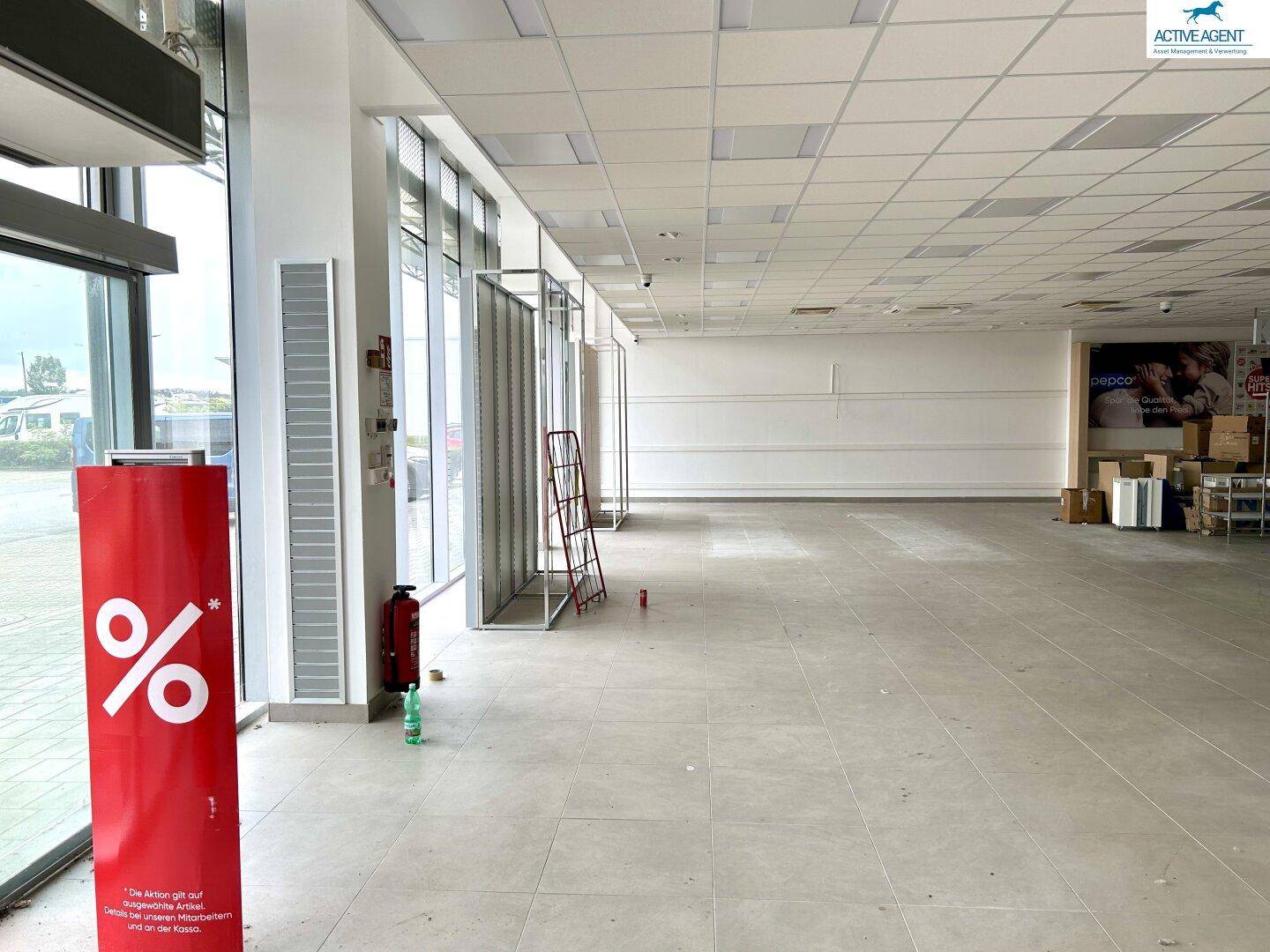 Großer, heller Verkaufsraum mit Fliesenboden und bodentiefen Fenstern, die viel Tageslicht hereinlassen.