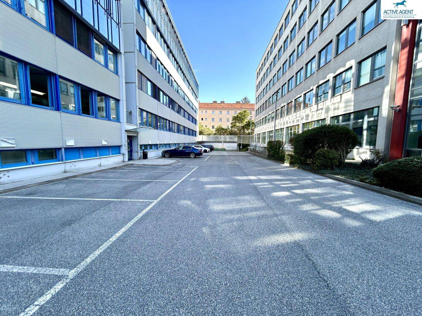 Außenparkplatz zwischen zwei modernen Bürogebäuden, bietet ausreichend Stellflächen für Fahrzeuge.