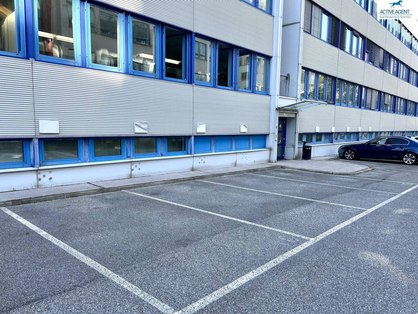 Weitere Außenparkplätze direkt am Gebäude, mit blauen Fensterrahmen und moderner Fassade.