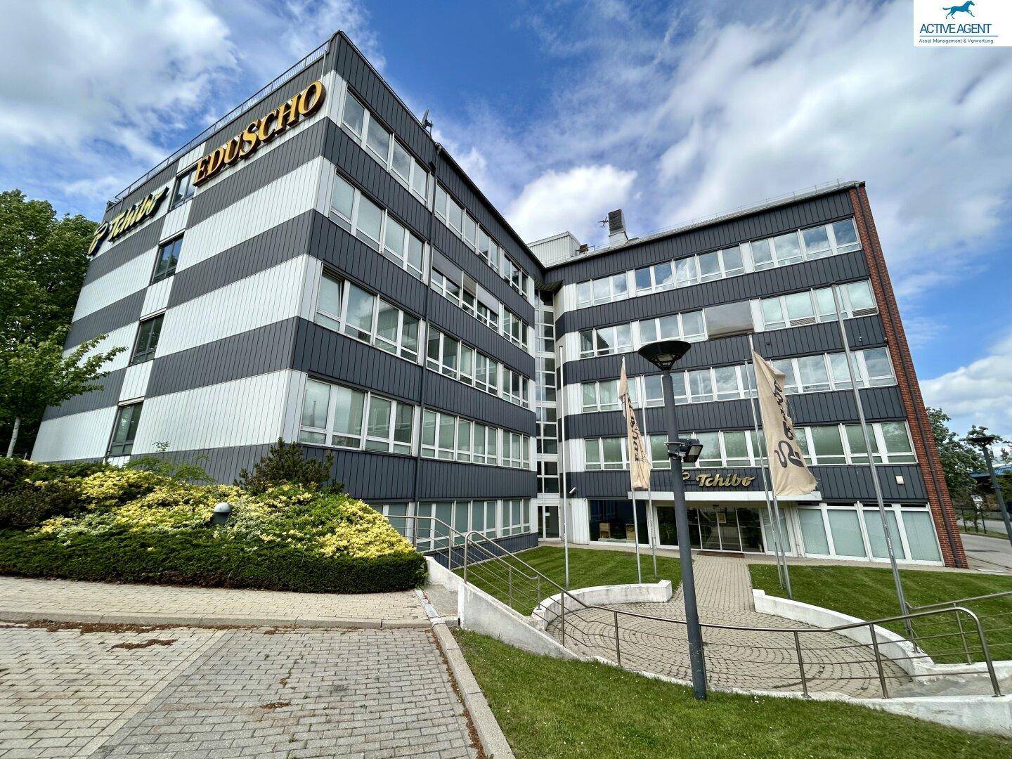 Weitwinkelansicht des modernen Bürogebäudes mit gestreifter Fassade, vielen Fenstern und einem hellen Himmel.